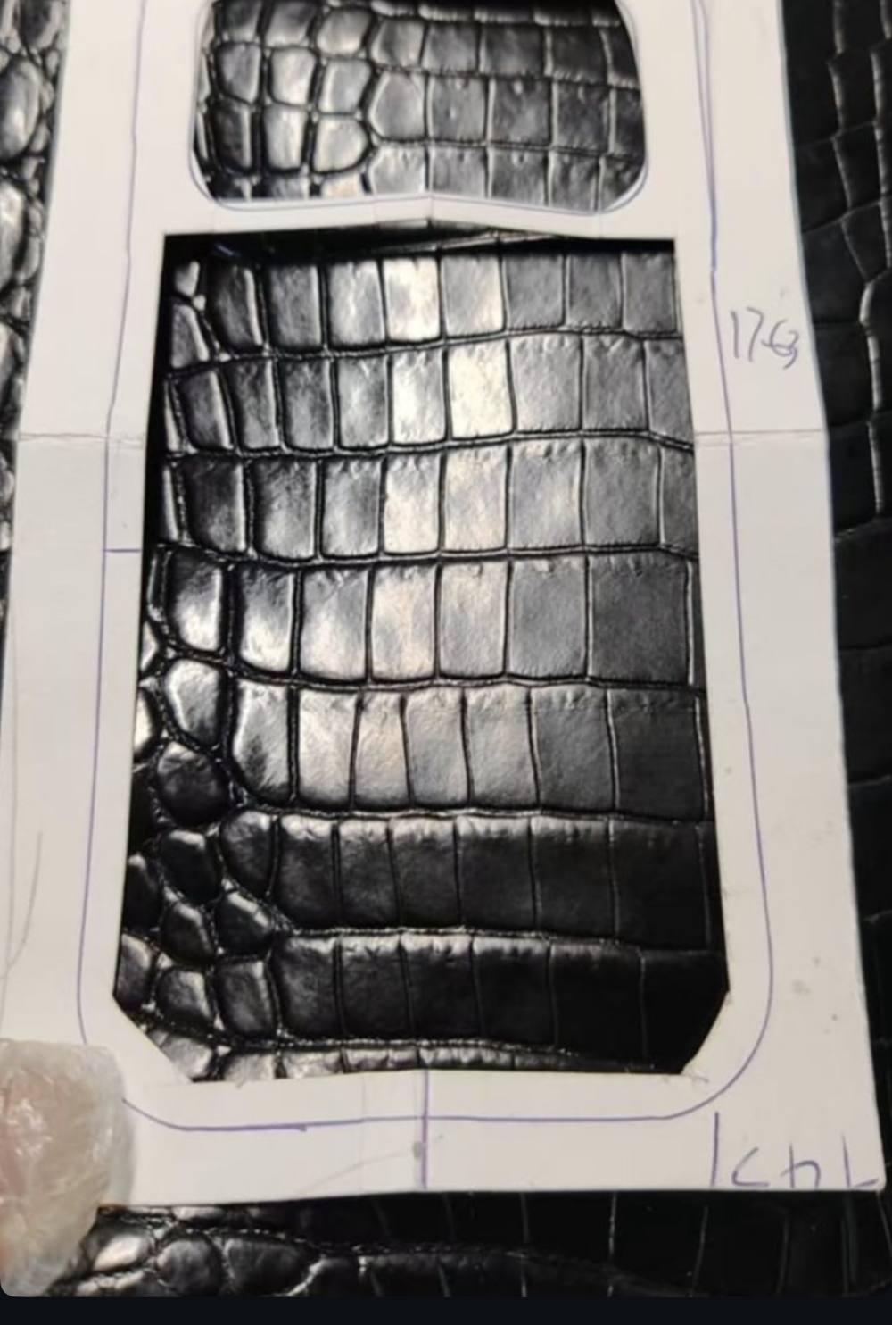 A paper cutting template laid over glossy black crocodile hide