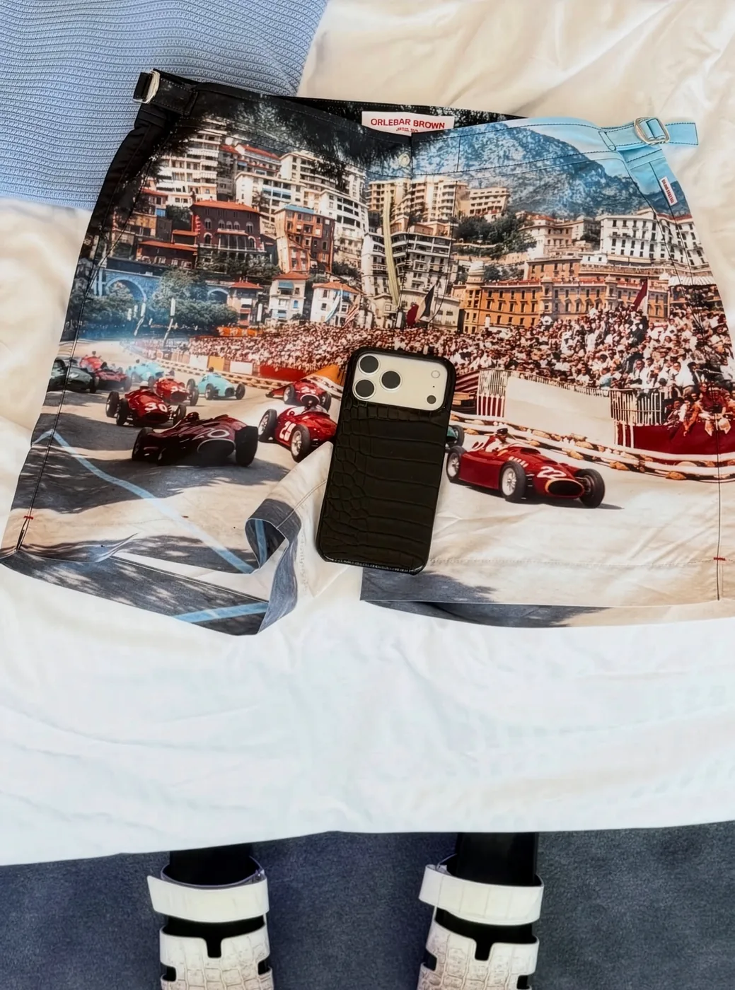 A black crocodile case resting on Monaco Grand Prix print shorts