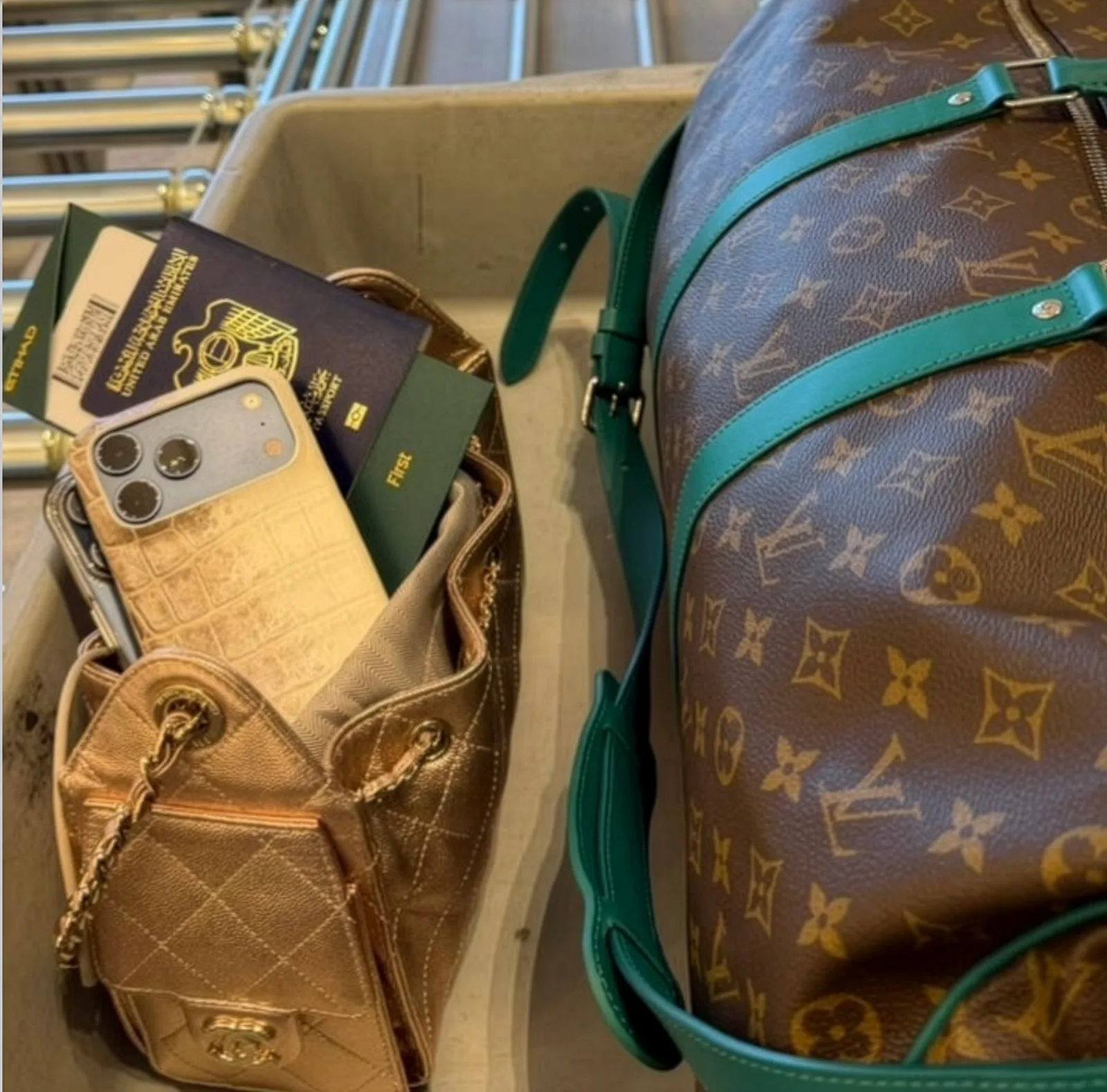A cream crocodile case and UAE passport tucked in a quilted bag beside a monogrammed duffle in an airport tray